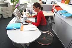 Themenfoto: Eine Frau im Rollstuhl arbeitet in einem Büro am PC