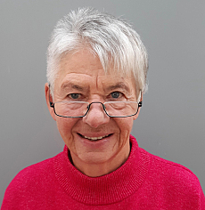 Portraitfoto von Sigrid Arnade. Sie hat kurze grau melierte Haare mit einer Strähne in die Stirn. Sie trägt einen roten Pullover mit hohem Halbschluss und lächelt über die Lesebrille hinweg in die Kamera