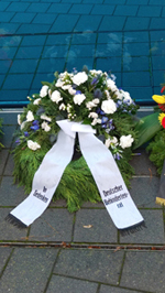 Kranz des Deutschen Behindertenrates mit weißen und einigen wenigen blauen Blumen. Die Schmuckschleife ist weiß mit schwarzer Schrift: 
