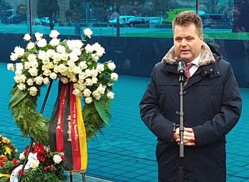 Jürgen Dusel vor der Blauen Wand der T4 Gedenkstätte, neben ihm ist der große Trauerkranz der Bundesregierung